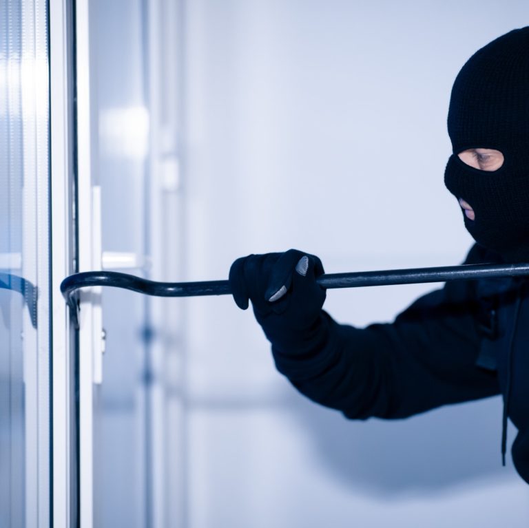 Robber in black balaclava cracking door with crowbar